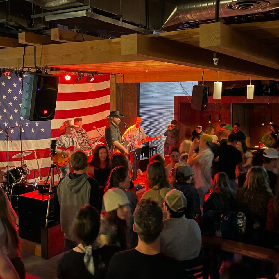 Crowded restaurant bar hosts a live band beneath a large American flag, with guests gathered around the dance floor.